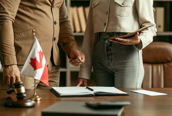 A Canadian flag alongside a professional office desk with laptop and documents representing work authorization during spousal sponsorship processing