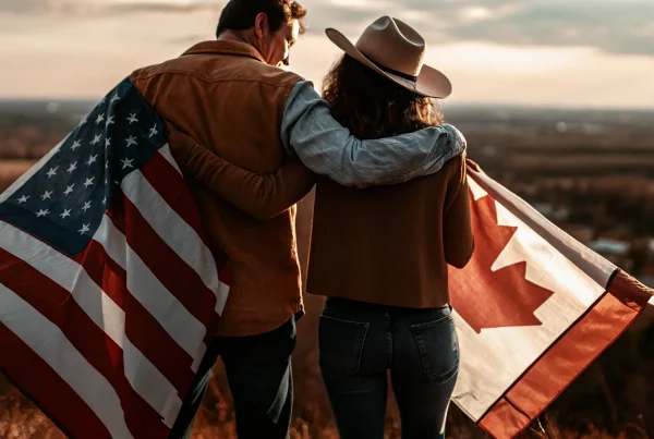 Canadian and American couple embracing at a border viewpoint with flags